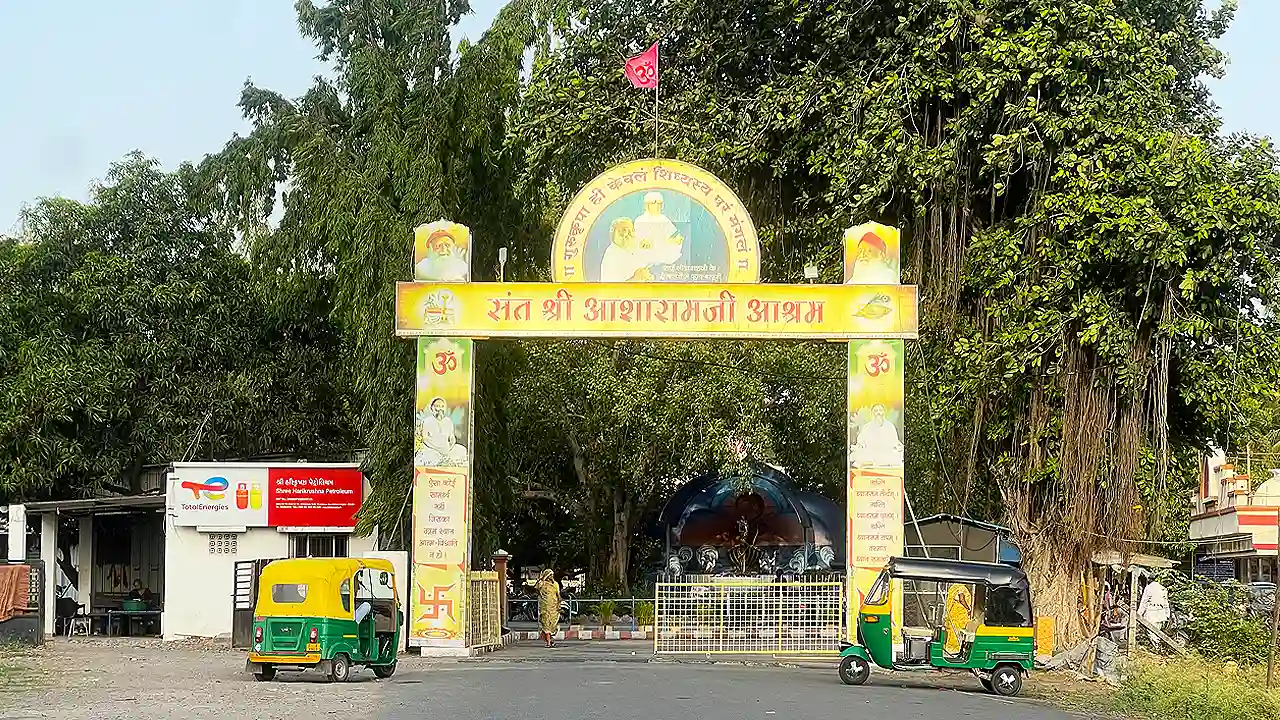Yellow arched main gate of Sant Shri Asharamji Ashram in Jahangirpura, with auto rickshaws parked and trees behind