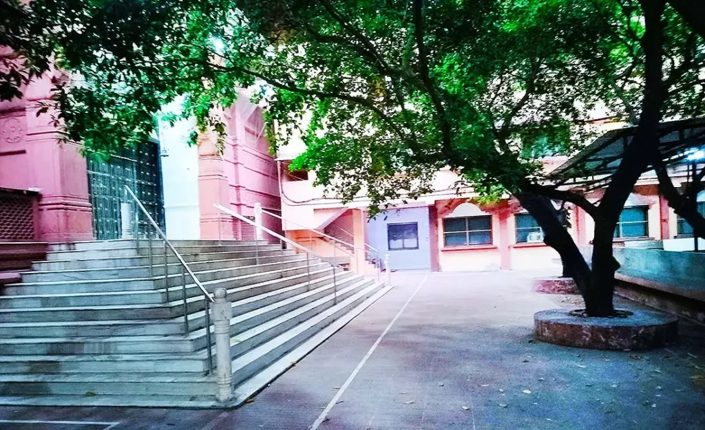 ISKCON Temple Surat back side with wide steps, metal railings and a large shady tree in the courtyard