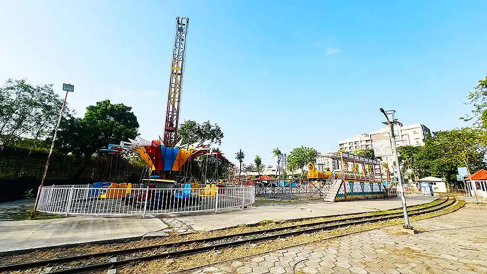 Rides and jhula games area at Botanical Garden Surat with train track visible in foreground