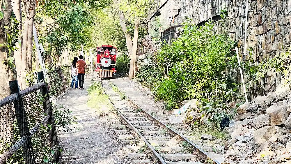 Red toy train running on track at Botanical Garden Surat with visitors standing nearby