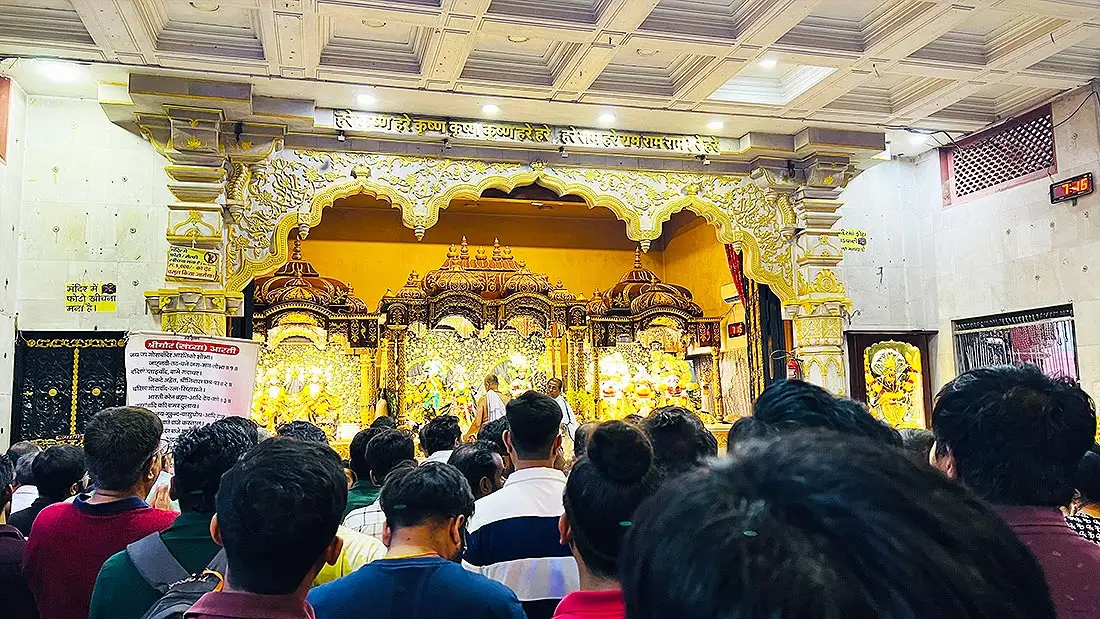 Golden altar with Radha Krishna murti at ISKCON Temple as devotees gather close for darshan