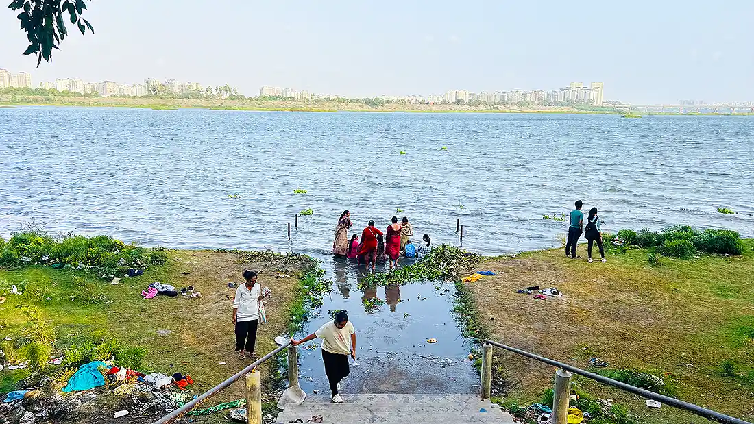 People bathing at the riverbank near the Jahangirpura ashram, with a city skyline across the wide river