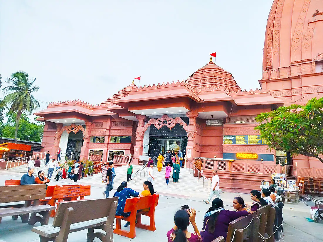 People resting on benches outside ISKCON Temple Jahangirpura as others walk down the temple steps