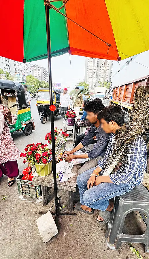 Roadside flower stall near Shyam Mandir on VIP Road, Surat, selling red roses and garlands under a colorful umbrella