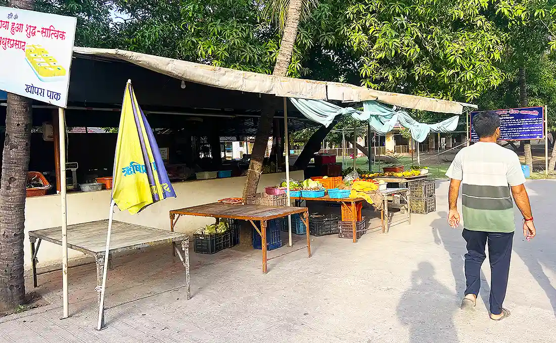 Vegetable and fruit stall at the Jahangirpura ashram with produce on tables under a shade, crates stacked below