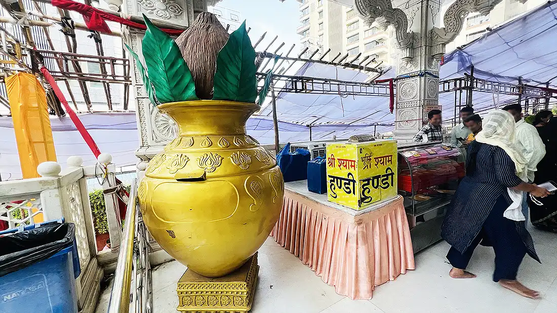 Large golden kalash with coconut and leaves near the entry of Shyam Baba temple, with Shri Shyam hundi boxes beside it