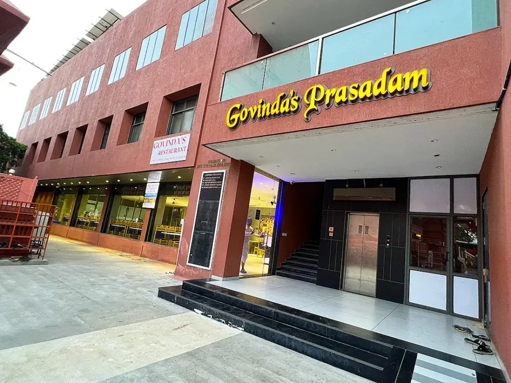 Govinda's Prasadam restaurant building at ISKCON Temple with yellow sign, glass dining area and lift