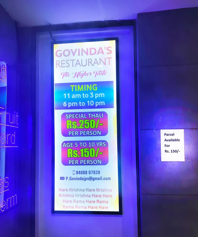Govinda's Restaurant board at ISKCON Temple showing timing, thali price, contact number and email