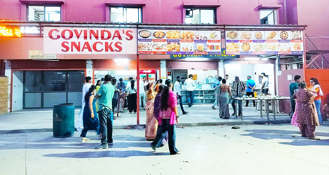 Govinda's Snacks food counter at ISKCON Temple with lit menu boards and visitors in the open courtyard