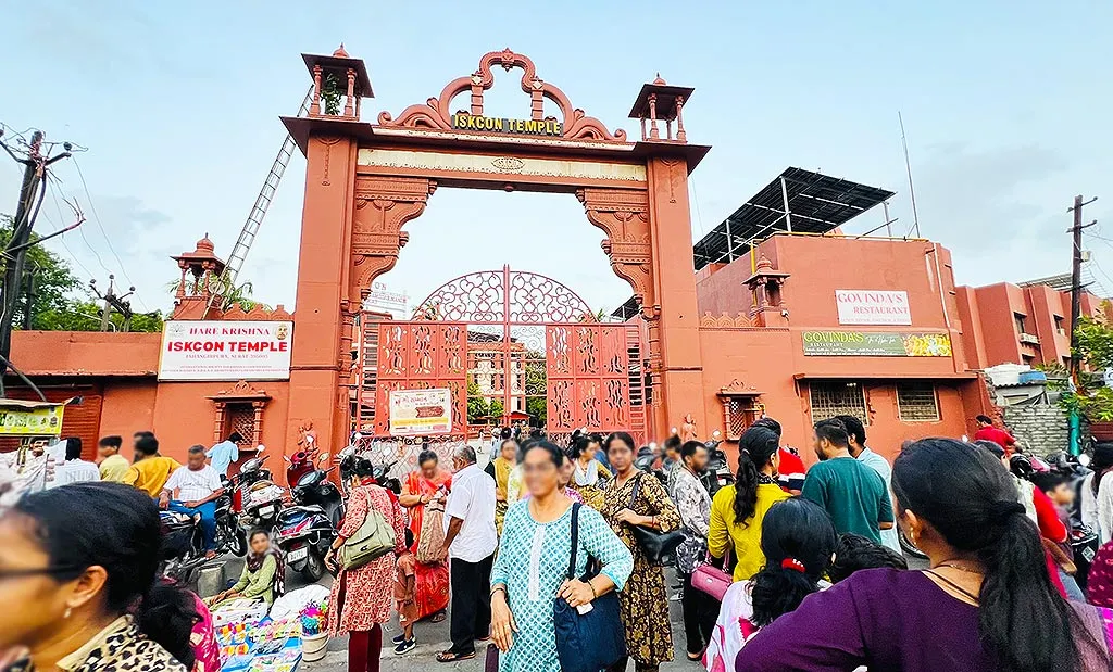 Red ISKCON Mandir Surat gate in Jahangirpura with visitors gathered outside and Govinda's Restaurant