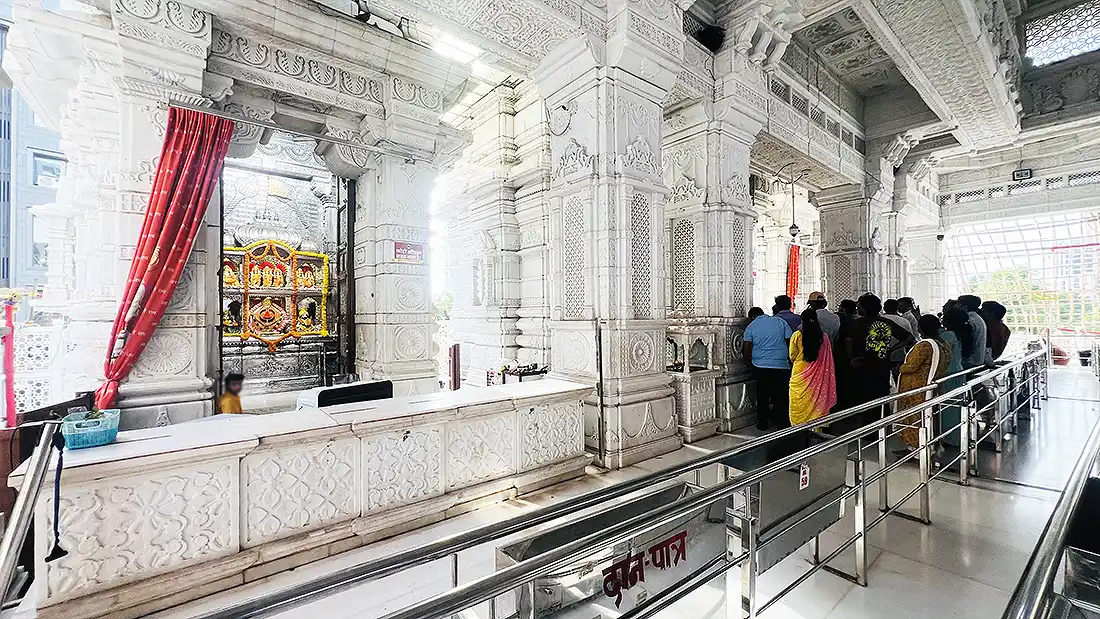 Carved white marble interior of Shyam Baba temple on VIP Road, with devotees queued along the railing for darshan