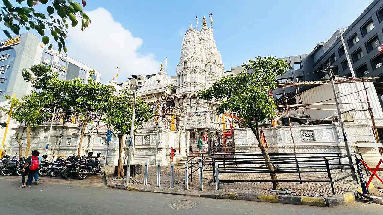Khatu Shyam Mandir Surat, a white marble temple with a tall carved spire, seen from the roadside with parked bikes
