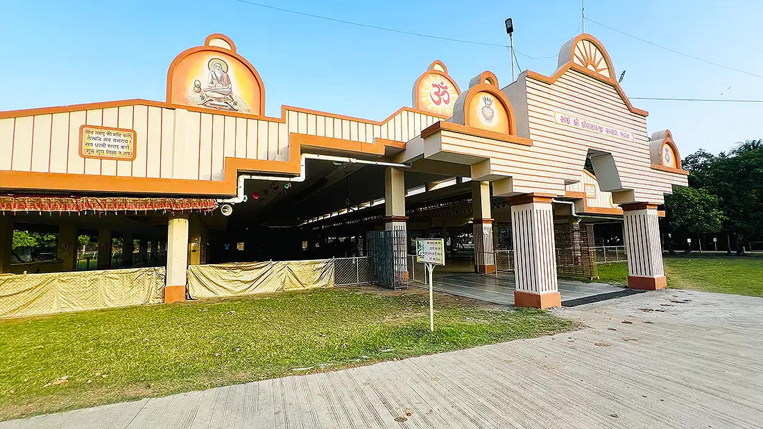 Satsang hall of the Jahangirpura ashram, a cream and orange open hall with Om and arched decorations along the roof