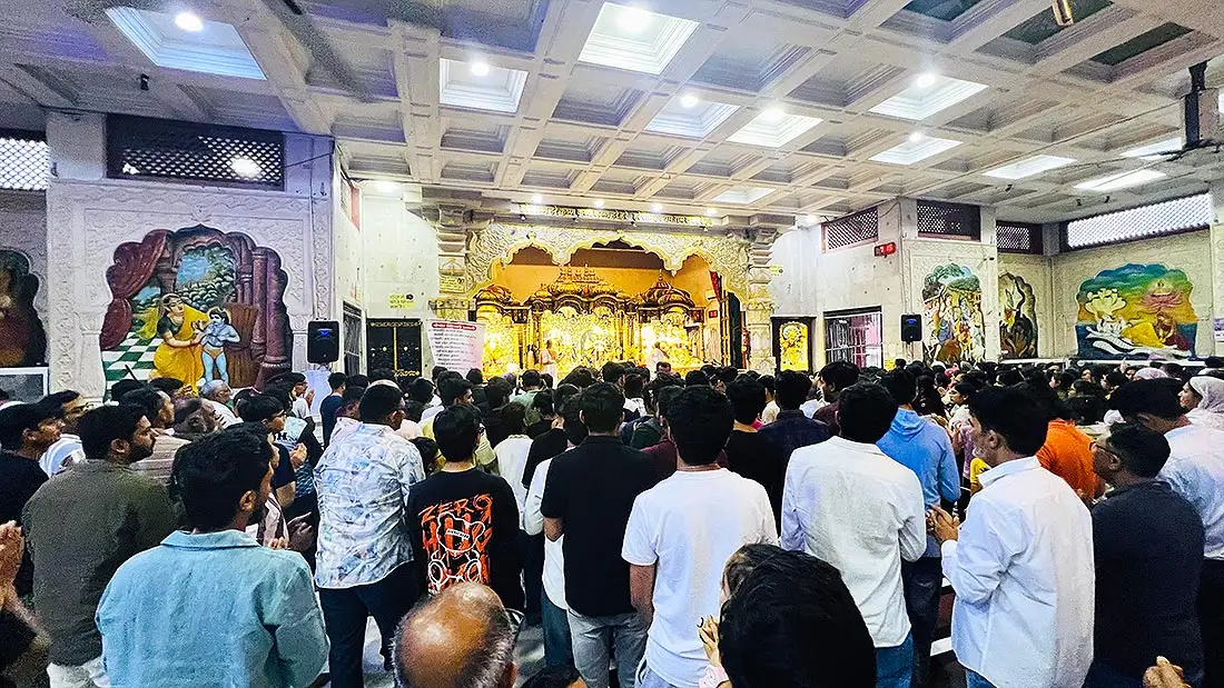 Male devotees standing before the golden altar in the men section at ISKCON Mandir with wall paintings