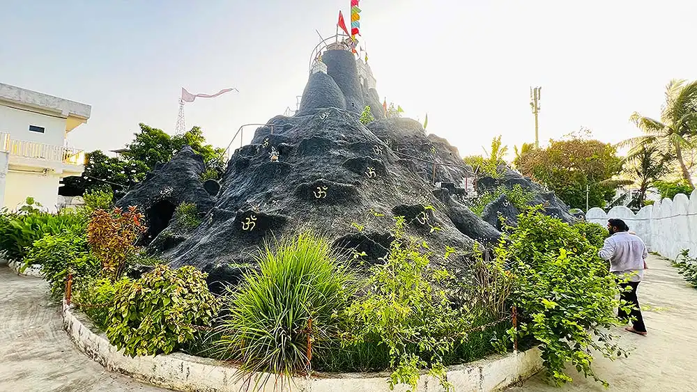 Mini Girnar rocky mountain structure behind Ram Madhi Surat with Om symbols and flags on top