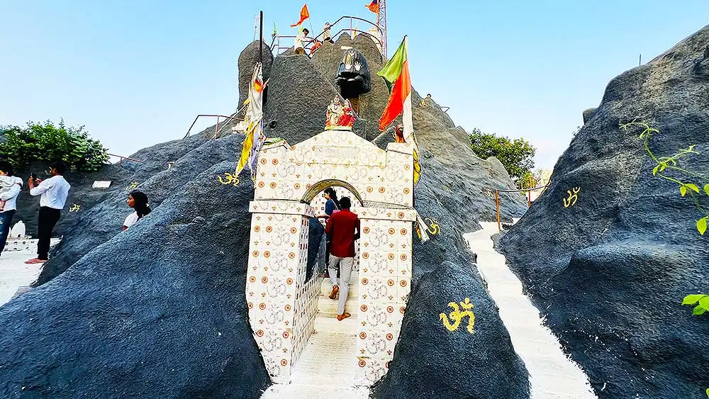 Visitors entering Mini Girnar Ram Madhi Surat through narrow rocky passage with Om symbols