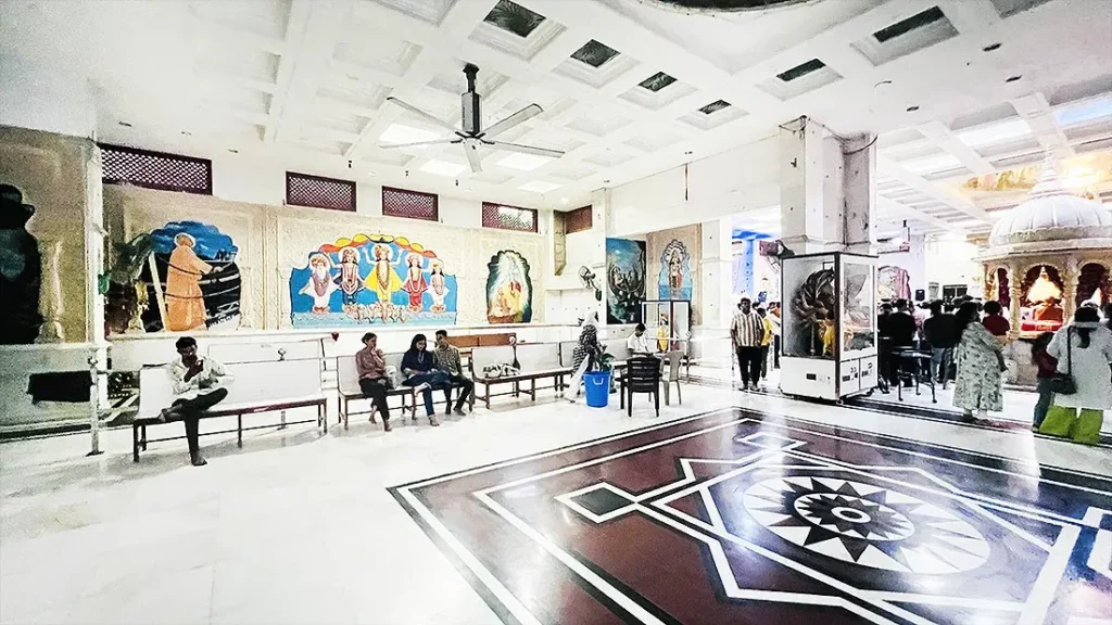 Second hall at ISKCON Temple with wall paintings, benches and a black star pattern on the marble floor