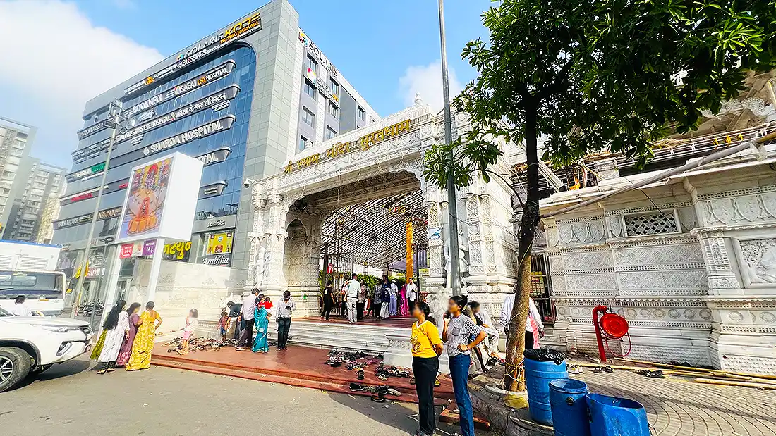 Carved marble entry gate of Shyam Baba Mandir near Vesu, Surat, with devotees gathered and shoes left outside