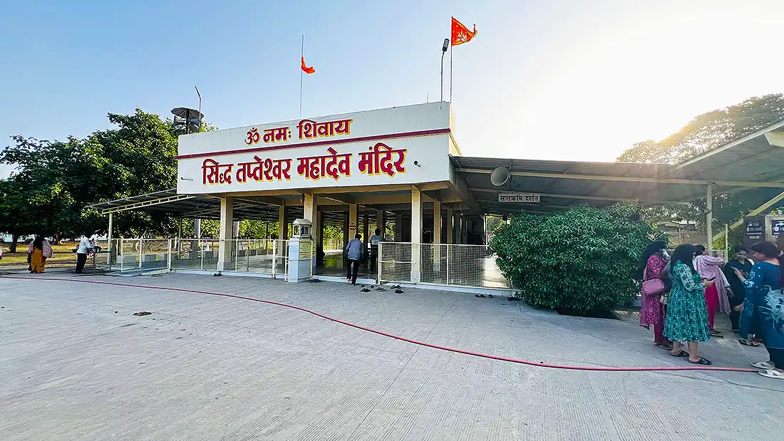 Siddha Tapteshwar Mahadev Mandir at the ashram, a small Shiva temple with red flags and devotees gathered outside