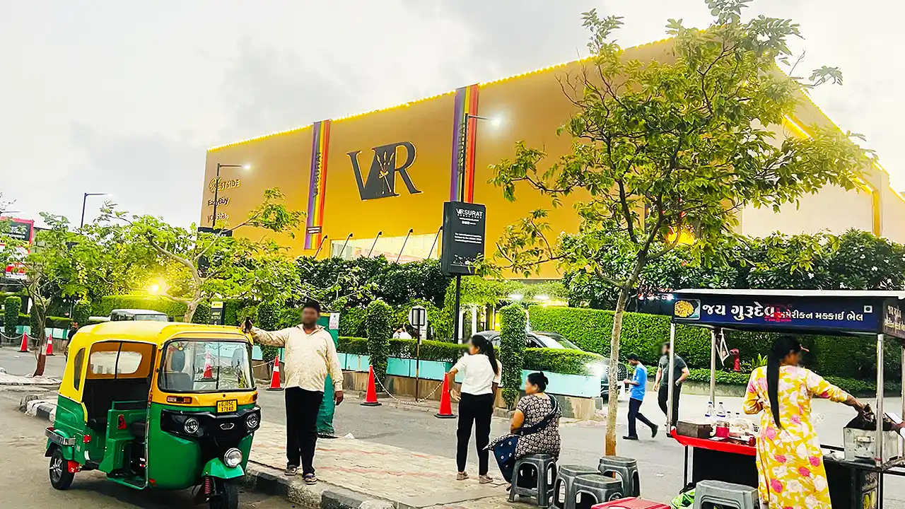 VR Mall Surat with its yellow VR facade, a green auto rickshaw parked in front and a roadside snack stall